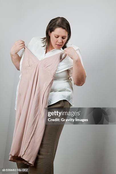 overweight women holding up small dress, looking down, close-up - heavy set women stock pictures, royalty-free photos & images