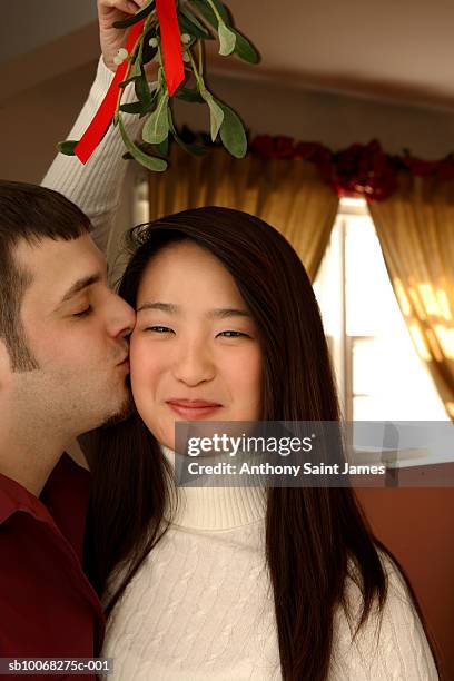 young couple kissing under mistletoe, smiling, close-up - anthony peck stock pictures, royalty-free photos & images