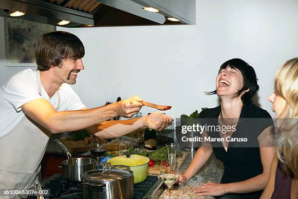 man preparing food for female friends in kitchen - kochen freunde stock-fotos und bilder