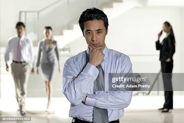 portrait of business man in lobby, others in background - adam weiss stock-fotos und bilder