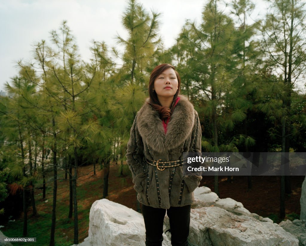 Young woman standing on rocks in park with eyes closed