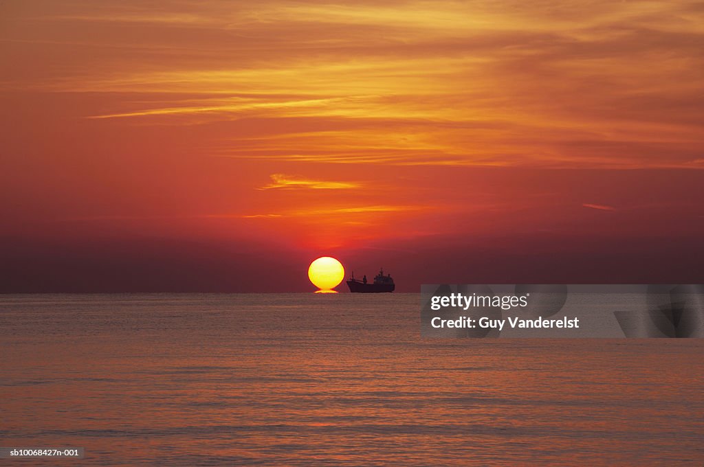 Ocean at sunset with silhouette of ship on horizon
