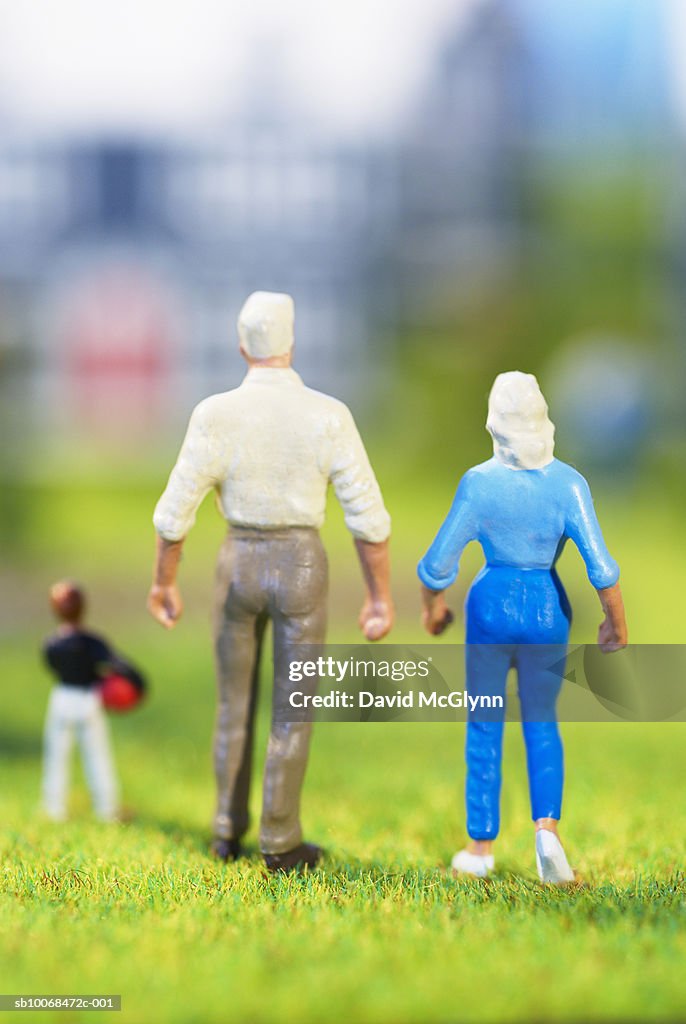 Figurines of family of three standing on grass, rear view, studio shot