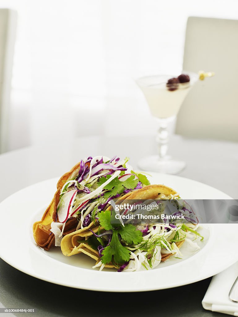 Fish tacos with cod, salsa verde, fennel and cabbage, cocktail in background