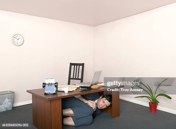 business man hiding under desk in miniature office - ropa tirada en el suelo fotografías e imágenes de stock