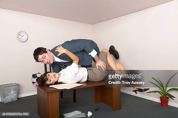 businessman and woman embracing on top of desk in office, portrait, side view - office small business stock-fotos und bilder