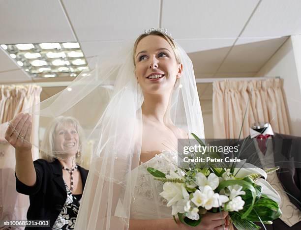 young woman wearing wedding dress, mature woman holding veil - wedding planning stockfoto's en -beelden