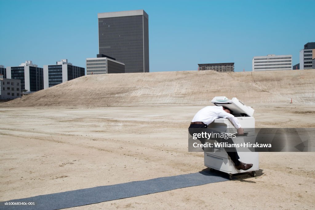 Man with head in copy machine on construction site, side view