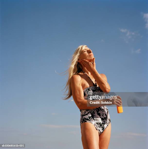 woman applying sun lotion, against blue sky - mature women skincare stock pictures, royalty-free photos & images