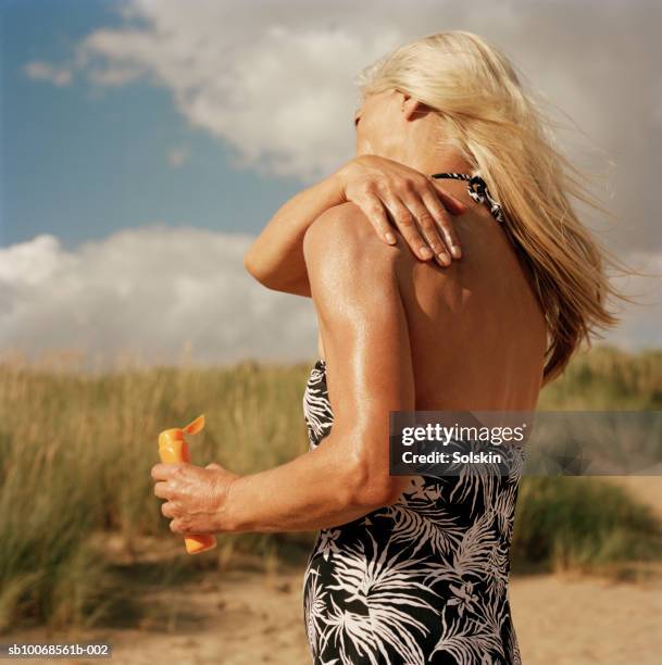 woman applying sun lotion on beach - middle aged woman bathing suit stock pictures, royalty-free photos & images