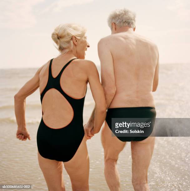 united kingdom, rye, camber sands, couple holding hands at ocean - badeanzug stock-fotos und bilder