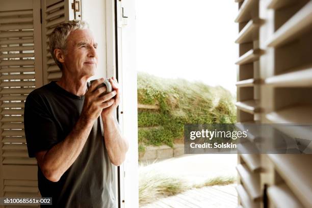 united kingdom, rye, camber sands, man holding drink in beach house - man having tea stock pictures, royalty-free photos & images