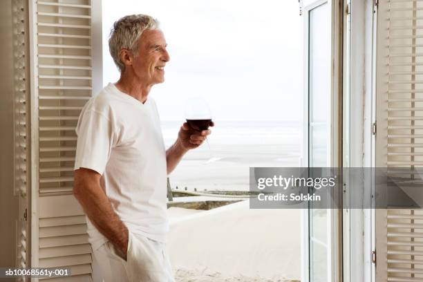 united kingdom, rye, camber sands, man holding drink in beach house doorway - beach house balcony fotografías e imágenes de stock