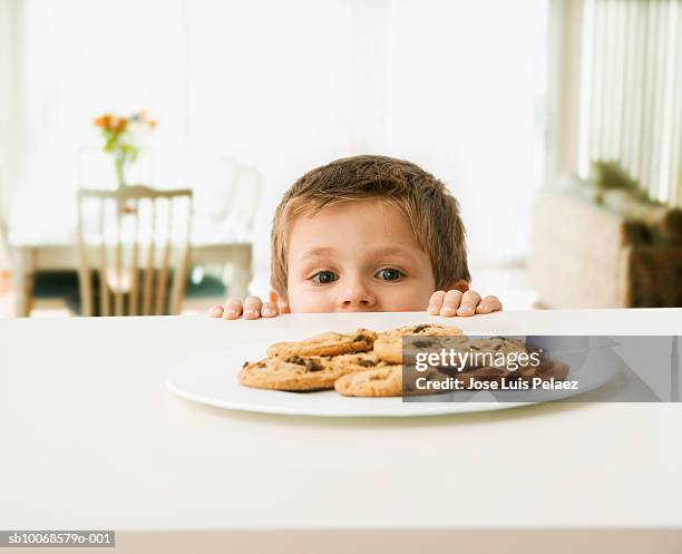 boy (3-4) looking at plate of cookies on table - kid peeking stock pictures, royalty-free photos & images