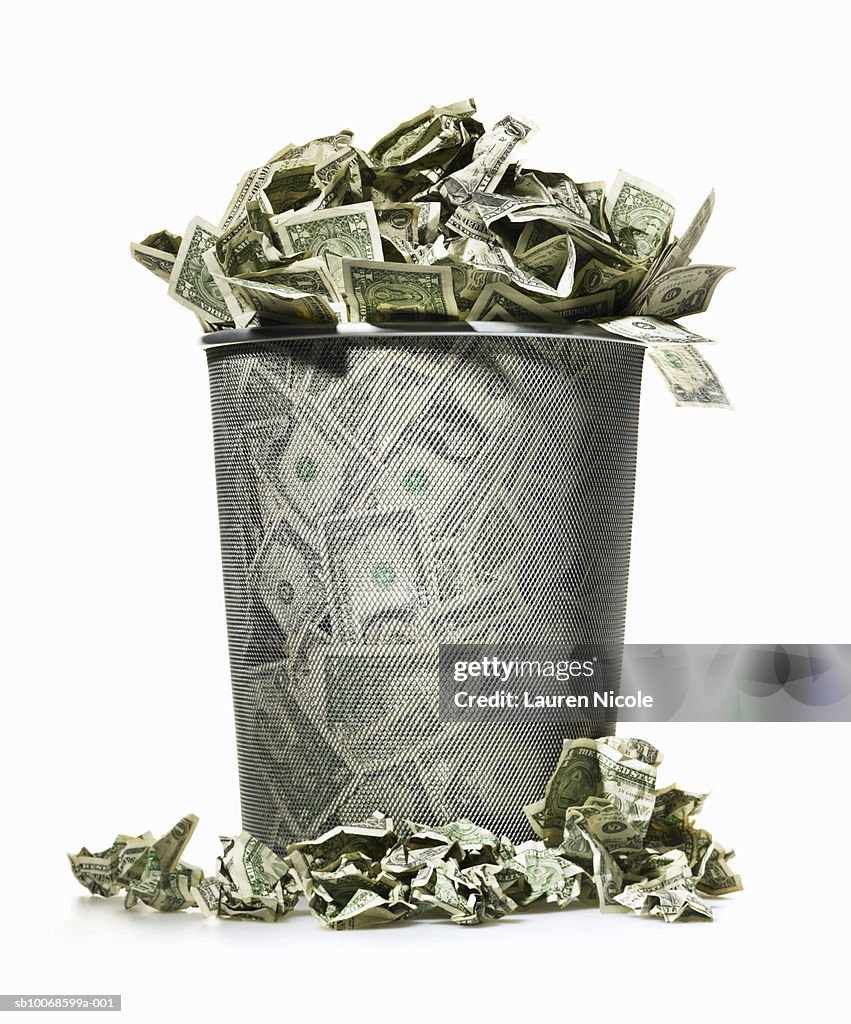 Dollar bills spilling out of wire waste basket