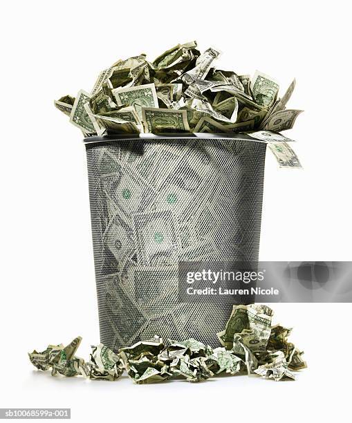 dollar bills spilling out of wire waste basket - waste wealth stock pictures, royalty-free photos & images