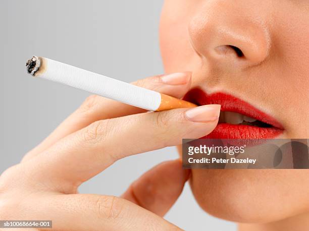 young woman wearing red lipstick smoking, close up on cigarette in mouth, studio shot - beautiful women smoking cigarettes stockfoto's en -beelden