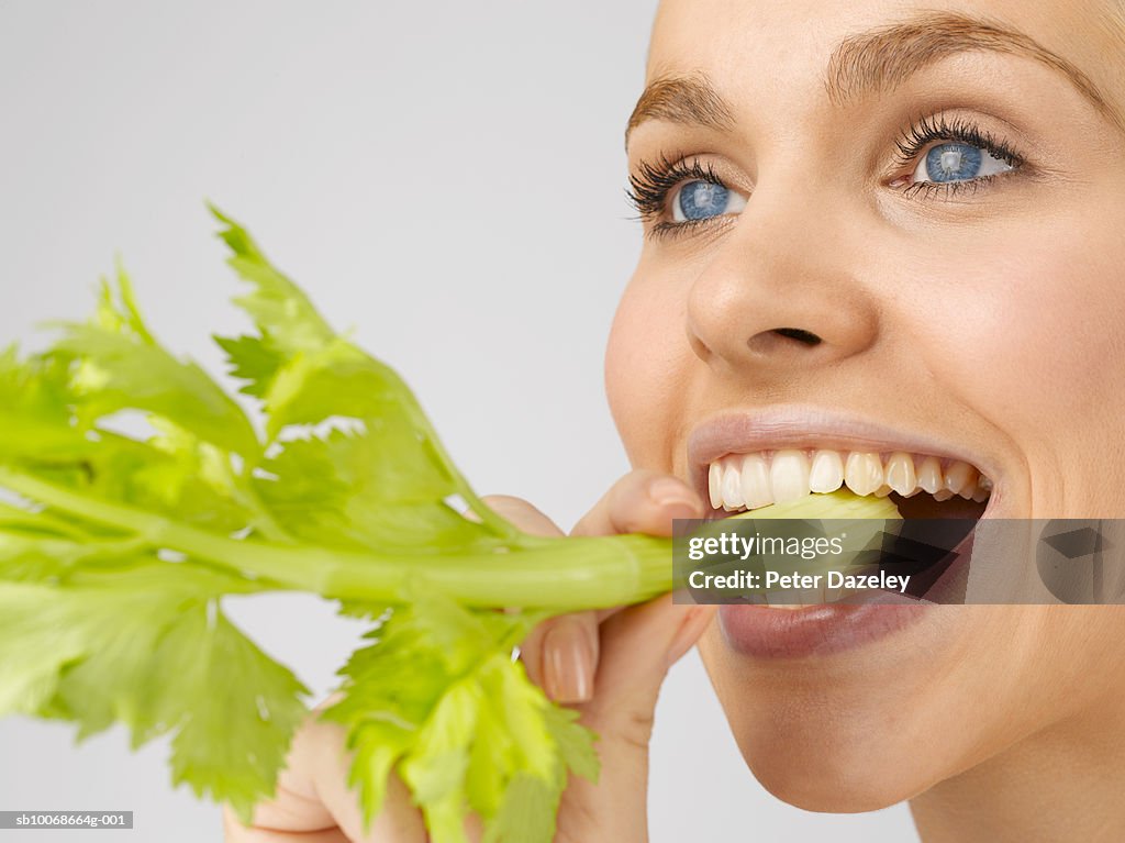 Young woman biting on celery stalk, close up, studio shot