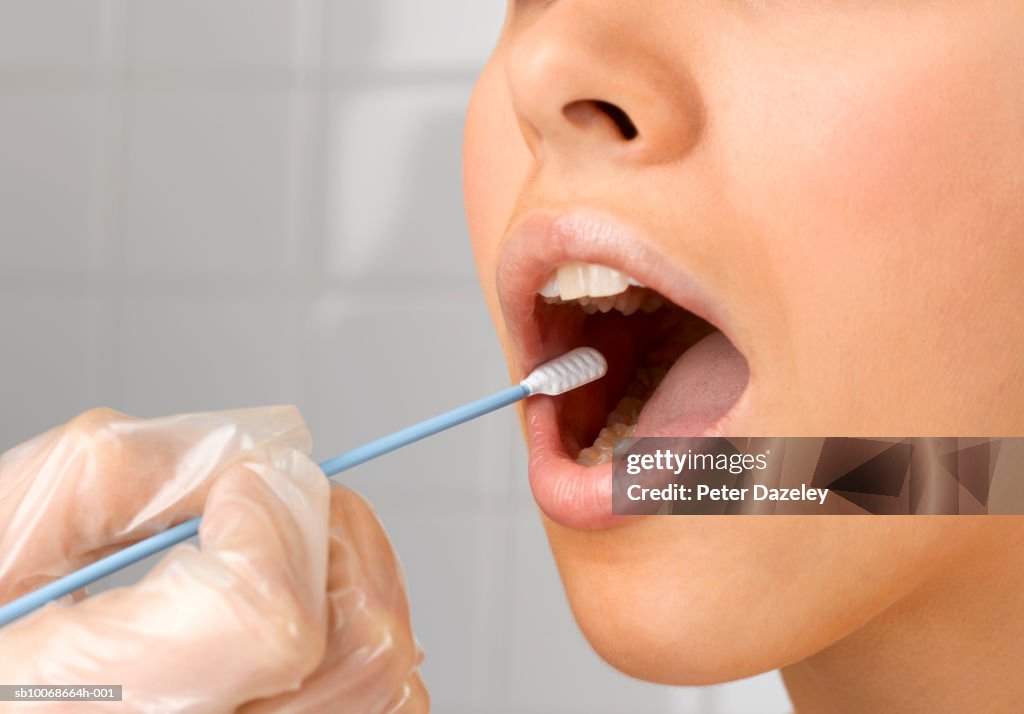 Person holding DNA swab in young woman's mouth, close up of mouth, studio shot