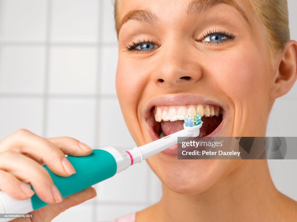 Young woman cleaning teeth with electric toothbrush, close up, studio shot