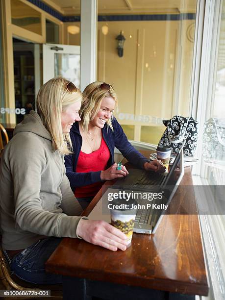 two young woman in caft using laptop, smiling, side view - caft stock pictures, royalty-free photos & images