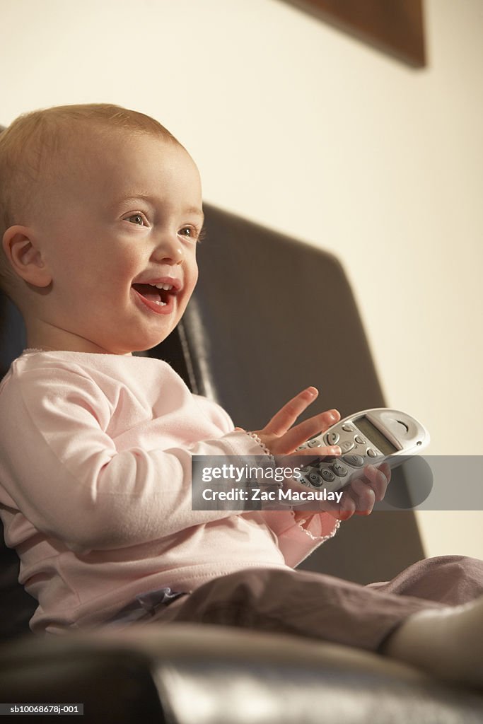 Baby girl (6-11 months) holding mobile phone sitting on chair, low angle view