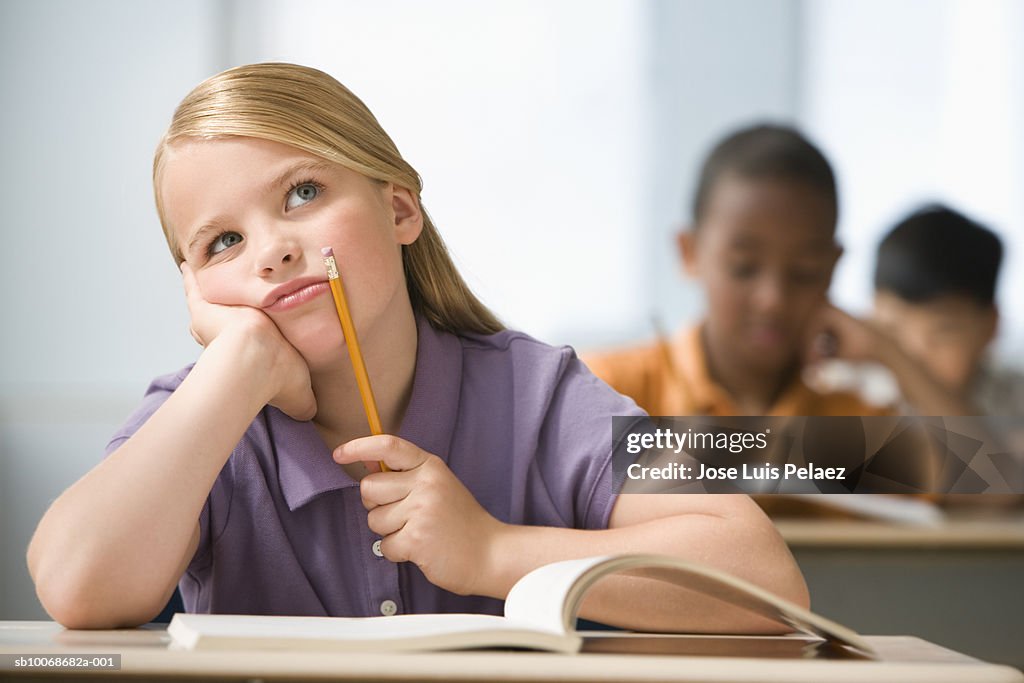 Girl (6-7) sitting in classroom with head in hands, students in background