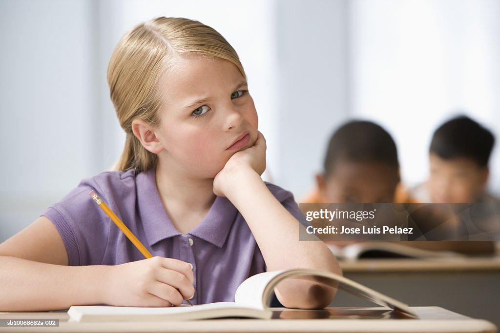 Girl (6-7) sitting in classroom with head in hands, students in background