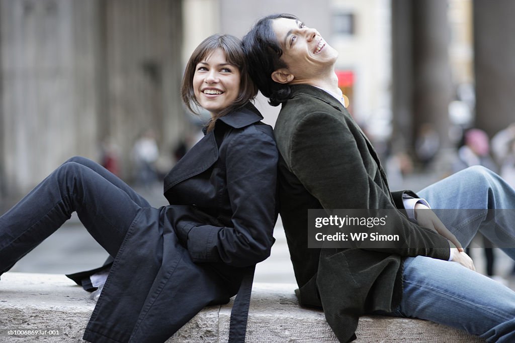 Italy, Rome, couple relaxing on wall back to back