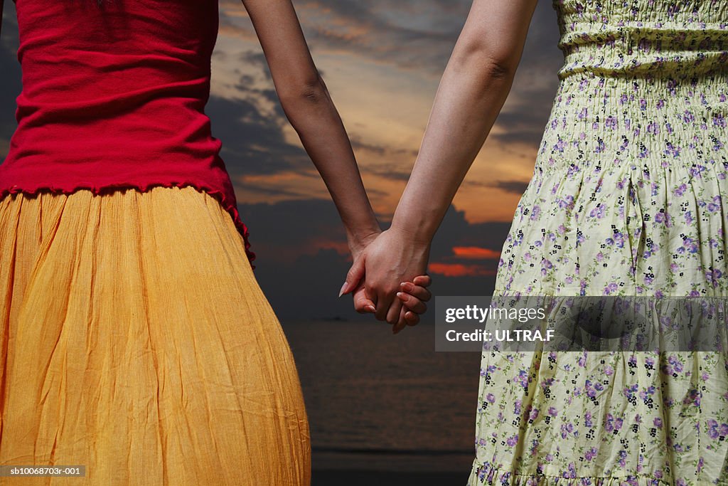 Two women holding hands, outdoors, mid section