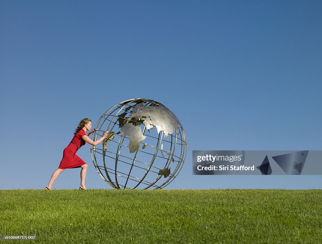 Woman pushing large metal-frame globe sculpture in grass field