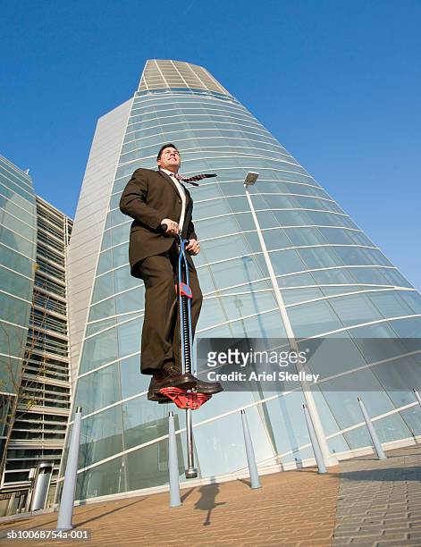 businessman jumping on pogo stick in front of convention center - pogo stock-fotos und bilder