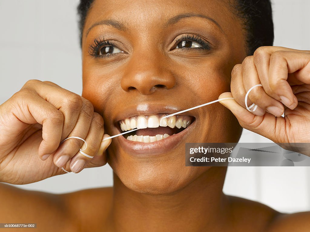Woman cleaning teeth with dental floss, close up, studio shot