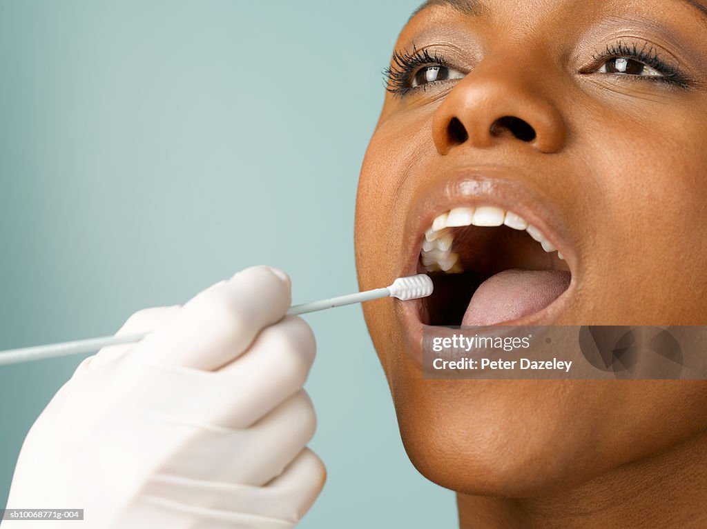 Person putting DNA test swab into woman's mouth, close up, studio shot