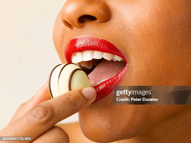 woman putting chocolate praline in mouth, close up, studio shot - chocolate pieces stock-fotos und bilder