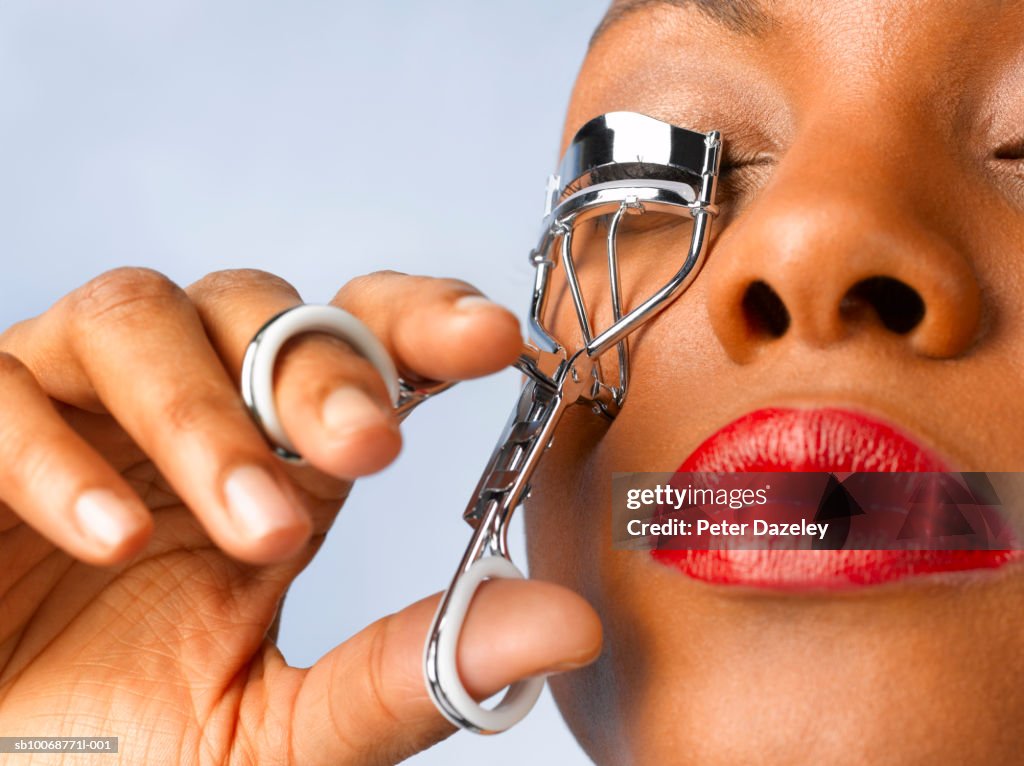 Woman using eyelash curler, close, studio shot