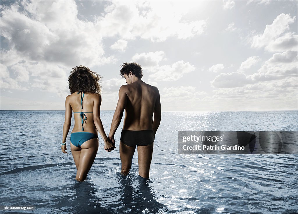 Young couple walking in sea, rear view