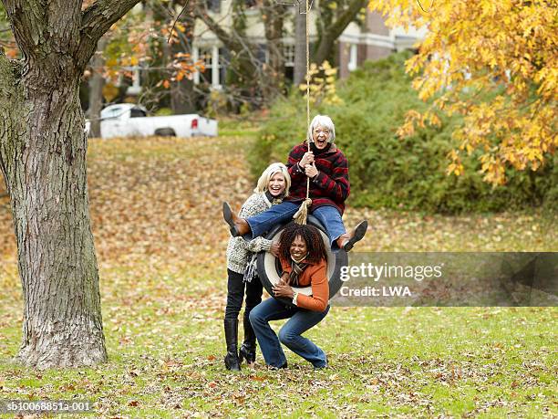 three women playing on tyre swing, portrait - the fall band stockfoto's en -beelden