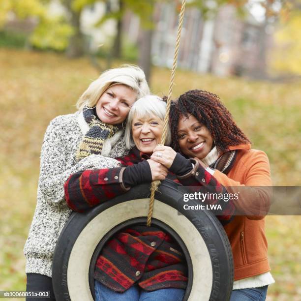 three women playing on tyre swing - the fall band stockfoto's en -beelden