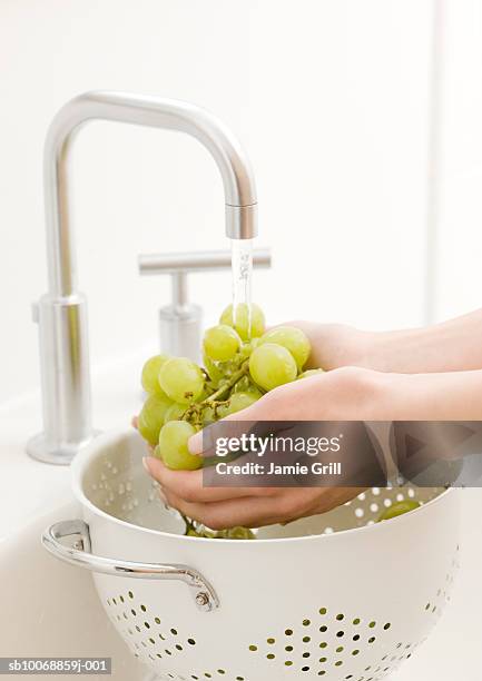 woman's hand washing grapes in kitchen sink - food waste stockfoto's en -beelden