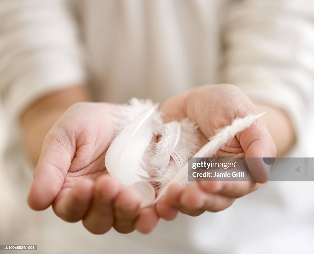 Child's hands holding feathers, close-up, mid section