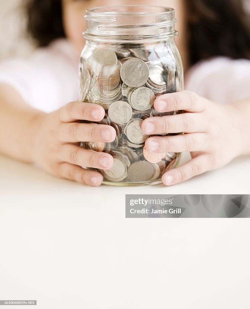 Child holding jar of coins, close-up, mid section