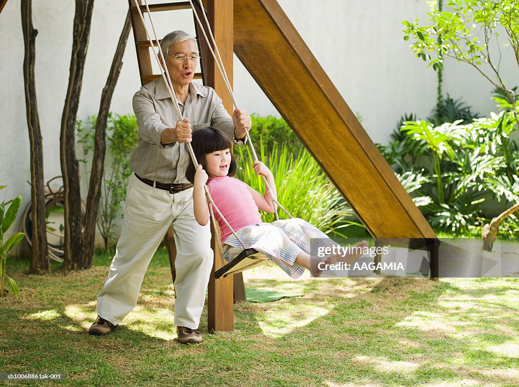 Grandfather playing with granddaughter (4-5) in park swing