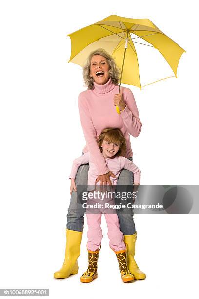 grandmother with granddaughter (4-7) holding umbrella, smiling - holding umbrella stock pictures, royalty-free photos & images
