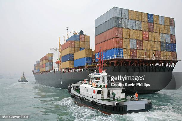china, hong kong harbor, tugboat sailing alongside container ship - container ship fotografías e imágenes de stock