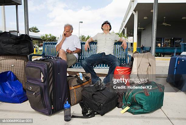 two men with luggage sitting in airport area - valises bagages stock-fotos und bilder