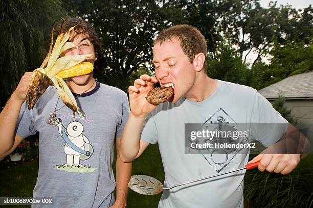 two men eating raw food in garden - burger on grill photos et images de collection