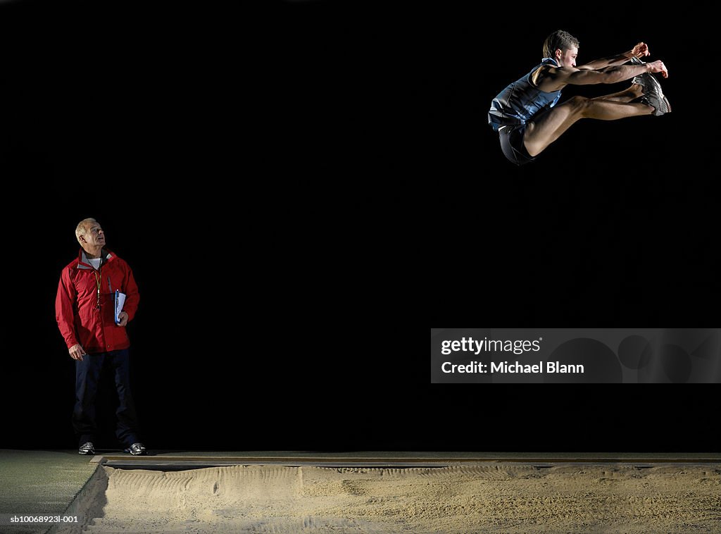 Long jump athlete jumping, coach watching