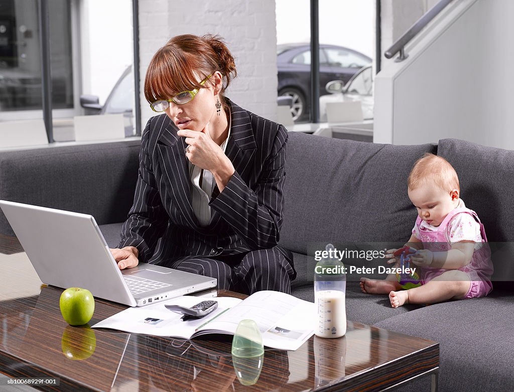 Mother working on laptop, baby boy (6-11 months) playing with toys