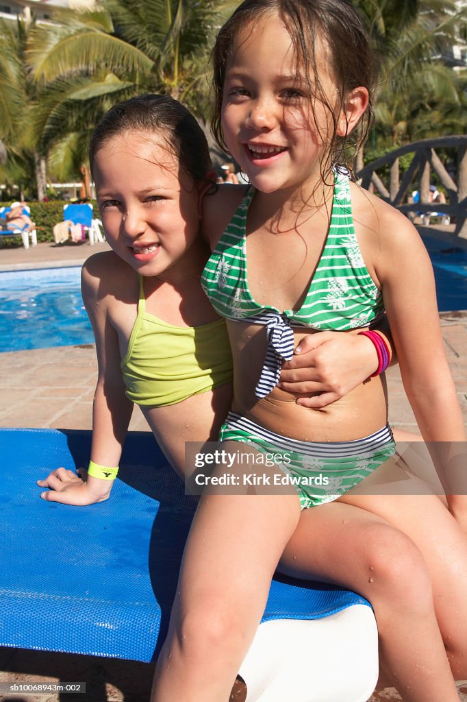 Two girls (4-7) sitting on lounge chair, smiling, portrait